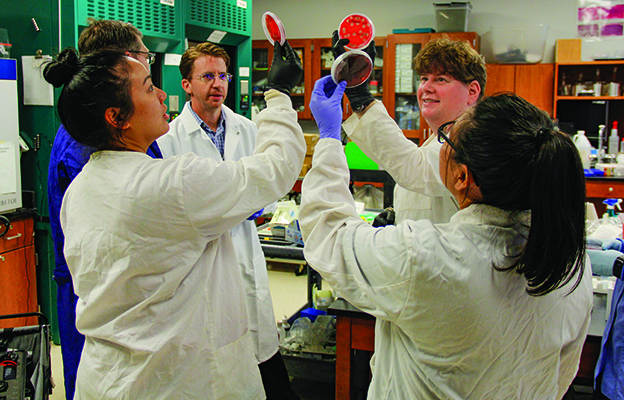 Health Sciences students in lab coats holding up petrie dishes